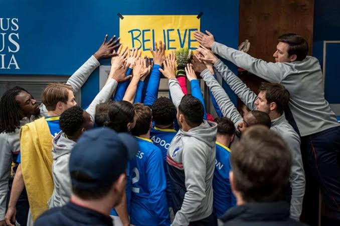 afc richmond players all around the yellow "believe" sign that it taped about the managers office door with their hands on it before a match